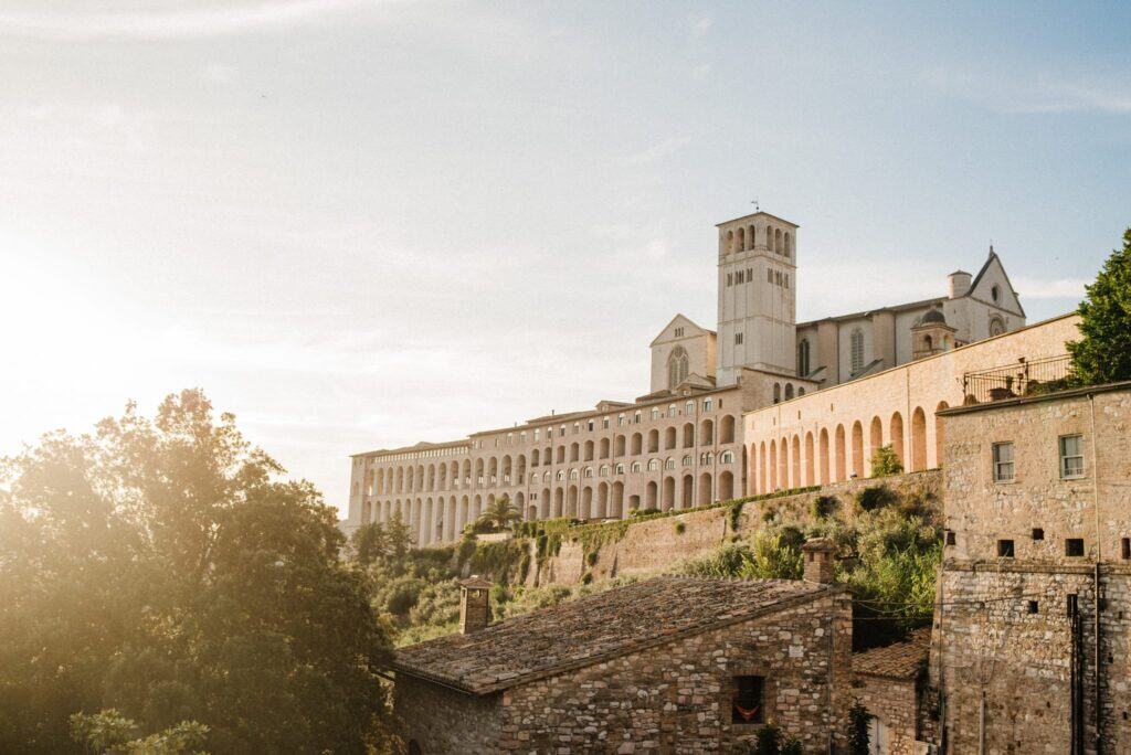 Ancient Italian monastery on a hillside with sunlit trees and historic stone buildings in Italy.